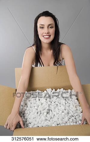 Stock Image - Portrait of a young woman holding a cardboard of packing peanuts and smiling. Fotosearch