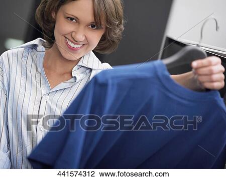 Portrait of a young woman holding a t-shirt on a hanger and smiling View Large Photo Image Stock Image - Portrait of a young woman holding a t-shirt on a hanger and smiling. Fotosearch