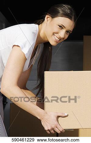 Stock Photo - Portrait of a young woman holding a cardboard box and smiling. Fotosearch