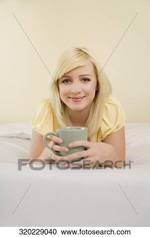 Portrait of a young woman lying on the bed and holding a tea cup View Large Photo Image Stock Image - Portrait of a young woman lying on the bed and holding a tea cup. Fotosearch
