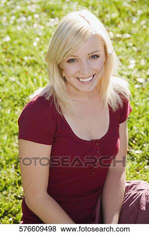 Stock Photo - Portrait of a young woman sitting in a park and smiling. Fotosearch
