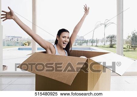 Portrait of a young woman sitting in a cardboard box with her arms raised View Large Photo Image Stock Photography - Portrait of a young woman sitting in a cardboard box with her arms raised. Fotosearch
