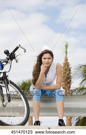 Stock Image - Portrait of a young woman sitting on a railing. Fotosearch