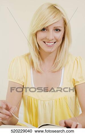 Stock Image - Portrait of a young woman sitting on the bed and reading a book. Fotosearch