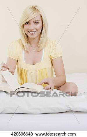 Portrait of a young woman sitting on the bed and reading a book View Large Photo Image Stock Photo - Portrait of a young woman sitting on the bed and reading a book. Fotosearch