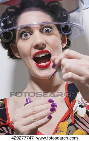 Portrait of a young woman sitting under hair dryer and applying nail polish View Large Photo Image Stock Photo - Portrait of a young woman sitting under hair dryer and applying nail polish. Fotosearch