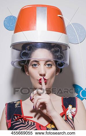 Portrait of a young woman sitting under hair dryer with her finger on her lips View Large Photo Image Stock Photography - Portrait of a young woman sitting under hair dryer with her finger on her lips. Fotosearch