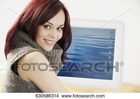 Picture - Portrait of a young woman smiling in front of a computer monitor. Fotosearch