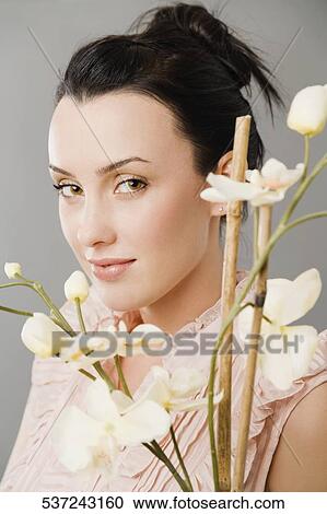 Stock Image - Portrait of a young woman smiling behind flowers. Fotosearch