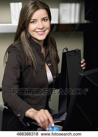 Portrait of a young woman using a credit card machine and holding a shopping bag View Large Photo Image Stock Photo - Portrait of a young woman using a credit card machine and holding a shopping bag. Fotosearch