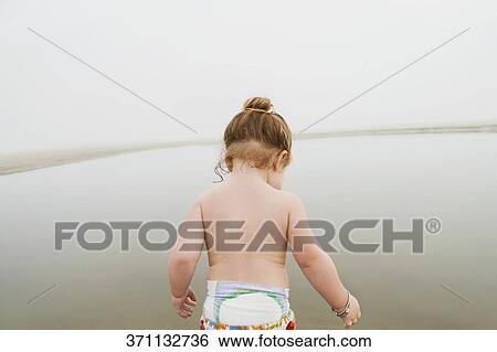 Rear view of a baby girl standing at the coast View Large Photo Image Stock Photograph - Rear view of a baby girl standing at the coast. Fotosearch