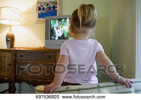 Stock Image - Rear view of a baby girl watching television. Fotosearch