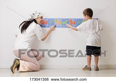 Rear view of a boy and his mother pasting wallpaper on the wall View Large Photo Image Stock Photograph - Rear view of a boy and his mother pasting wallpaper on the wall. Fotosearch