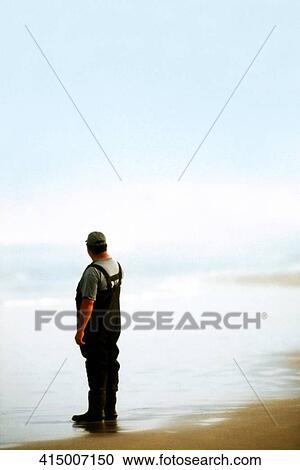 Stock Image - Rear view of a man standing on the beach and looking at view. Fotosearch