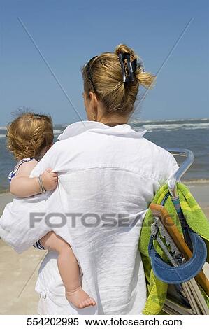 Rear view of a mid adult woman carrying her baby and holding a chair View Large Photo Image Stock Photography - Rear view of a mid adult woman carrying her baby and holding a chair. Fotosearch