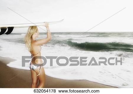 Rear view of a young woman carrying a surfboard on the beach View Large Photo Image Stock Photo - Rear view of a young woman carrying a surfboard on the beach. Fotosearch