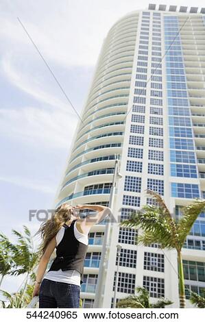 Rear view of a young woman looking at a skyscraper View Large Photo Image Stock Photography - Rear view of a young woman looking at a skyscraper. Fotosearch