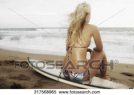 Rear view of a young woman sitting on a surfboard on the beach View Large Photo Image Stock Photography - Rear view of a young woman sitting on a surfboard on the beach. Fotosearch
