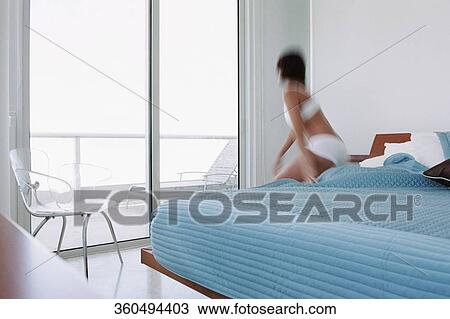 Stock Image - Rear view of a young woman waking up from the bed. Fotosearch
