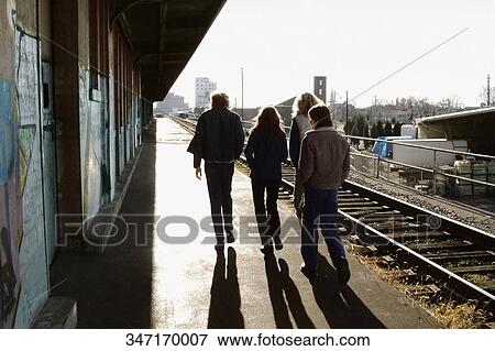Stock Photo - Rear view of three men with a woman walking at a railway station. Fotosearch
