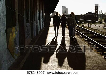Rear view of three men with a woman walking at a railway station View Large Photo Image Stock Photo - Rear view of three men with a woman walking at a railway station. Fotosearch