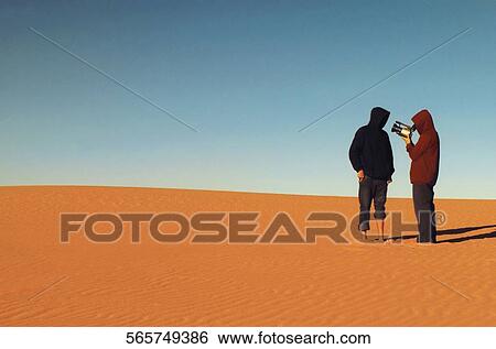 Stock Photograph - Rear view of two people standing in a desert and using a home video camera, Lake Mead, Utah, USA. Fotosearch