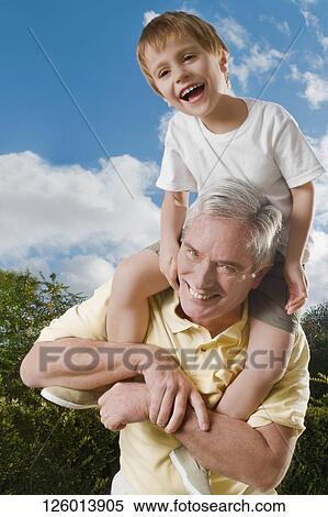Stock Photography - Senior man carrying his grandson on his shoulders and smiling. Fotosearch