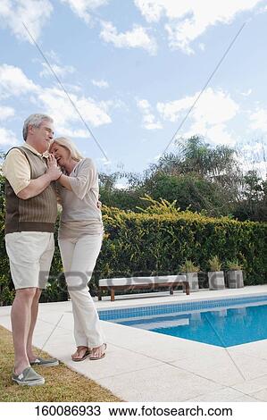 Stock Image - Senior man hugging a mature woman at the poolside and smiling. Fotosearch