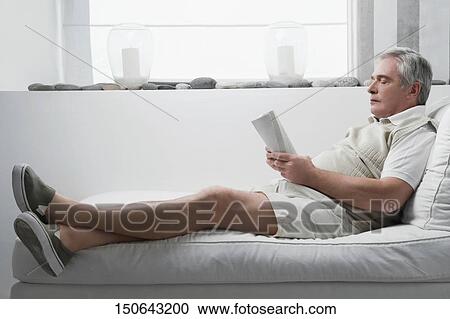 Stock Image - Senior man reclining on a chaise lounge and holding a book. Fotosearch