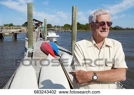 Stock Image - Senior man standing on a pier with his arms crossed. Fotosearch
