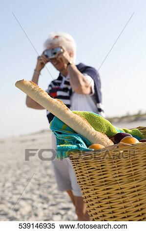 Senior woman standing near a basket and taking a picture with a camera on the beach View Large Photo Image Stock Photography - Senior woman standing near a basket and taking a picture with a camera on the beach. Fotosearch