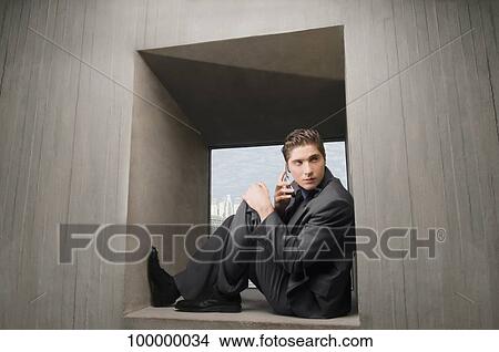 Side profile of a businessman sitting on a window sill and talking on a mobile phone View Large Photo Image Picture - Side profile of a businessman sitting on a window sill and talking on a mobile phone. Fotosearch