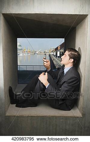 Side profile of a businessman sitting on a window sill and operating a mobile phone View Large Photo Image Stock Photography - Side profile of a businessman sitting on a window sill and operating a mobile phone. Fotosearch