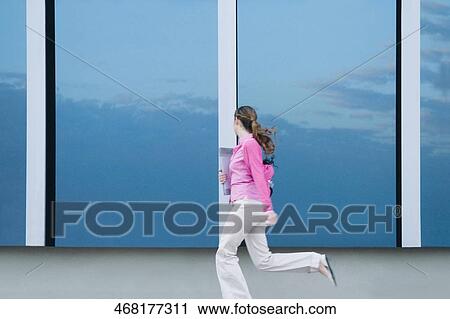 Stock Image - Side profile of a businesswoman running in the corridor of an office. Fotosearch