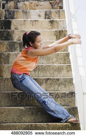 Stock Photography - Side profile of a girl holding a railing and standing on the staircase. Fotosearch