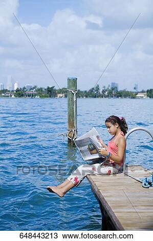 Side profile of a girl sitting on the pier and reading a newspaper View Large Photo Image Stock Image - Side profile of a girl sitting on the pier and reading a newspaper. Fotosearch