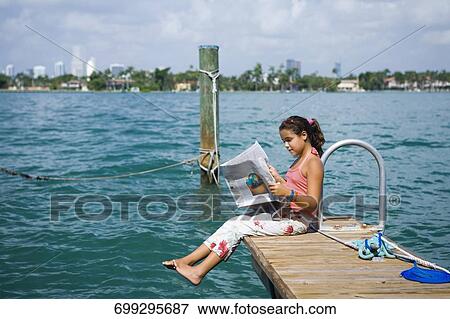 Side profile of a girl sitting on the pier and reading a newspaper View Large Photo Image Stock Photo - Side profile of a girl sitting on the pier and reading a newspaper. Fotosearch