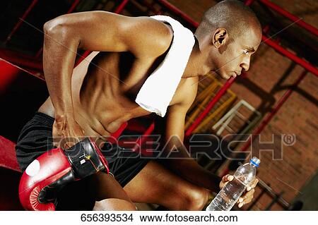 Picture - Side profile of a male boxer holding a water bottle and thinking. Fotosearch