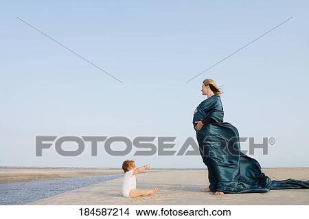 Side profile of a pregnant woman standing on the beach with her baby girl sitting in front of her View Large Photo Image Picture - Side profile of a pregnant woman standing on the beach with her baby girl sitting in front of her. Fotosearch