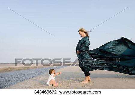 Side profile of a pregnant woman standing on the beach with her baby girl sitting in front of her View Large Photo Image Stock Image - Side profile of a pregnant woman standing on the beach with her baby girl sitting in front of her. Fotosearch