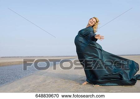 Stock Image - Side profile of a pregnant woman standing with her arms outstretched and smiling. Fotosearch