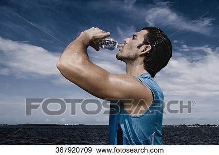 Stock Photo - Side profile of a young man drinking water from a water bottle. Fotosearch