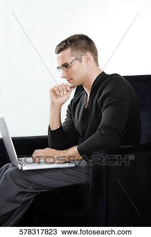Side profile of a young man sitting in an armchair and working on a laptop View Large Photo Image Stock Image - Side profile of a young man sitting in an armchair and working on a laptop. Fotosearch