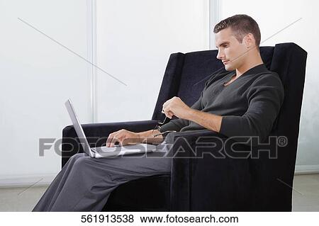 Side profile of a young man sitting in an armchair and working on a laptop View Large Photo Image Stock Photo - Side profile of a young man sitting in an armchair and working on a laptop. Fotosearch