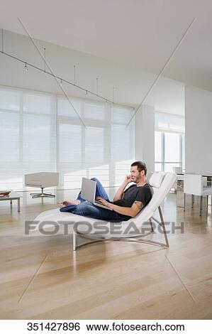 Side profile of a young man using a laptop and talking on a mobile phone View Large Photo Image Stock Photograph - Side profile of a young man using a laptop and talking on a mobile phone. Fotosearch