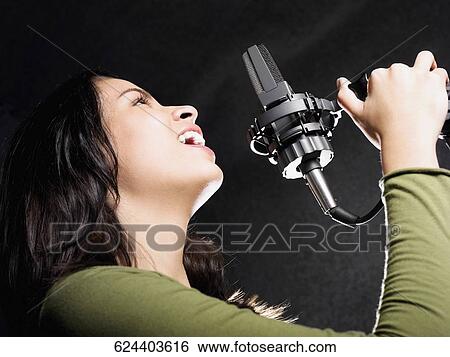 Side profile of a young woman holding a microphone and singing View Large Photo Image Stock Photograph - Side profile of a young woman holding a microphone and singing. Fotosearch