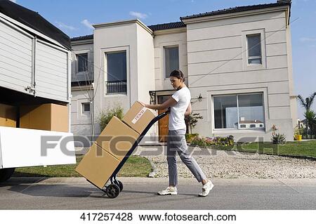 Side profile of a young woman pushing a push cart with cardboard boxes View Large Photo Image Stock Photo - Side profile of a young woman pushing a push cart with cardboard boxes. Fotosearch