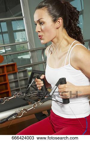 Stock Image - Side profile of a young woman exercising in the gym. Fotosearch