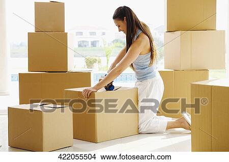 Side profile of a young woman taping cardboard boxes View Large Photo Image Picture - Side profile of a young woman taping cardboard boxes. Fotosearch