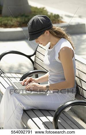 Stock Image - Side profile of a young woman using a laptop. Fotosearch